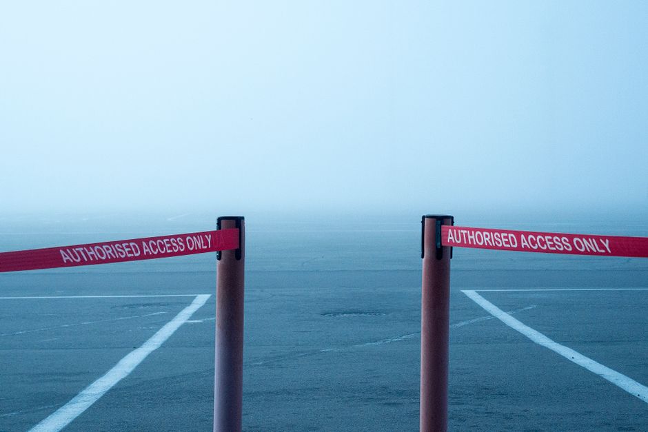 Two pink posts with red and white 'Authorised Access Only' tape strung between them block the entrance to a parking area or driveway, which is surrounded by foggy weather conditions. The pavement beneath the posts shows faint white lines marking parking spaces. The dense fog obscures visibility beyond the barriers, creating a restricted access zone likely used for home relocation or furniture transport purposes. This scene reflects a situation where access is limited, possibly during a moving or delivery process managed by a professional removals company such as Movers Harringay, whose services include careful planning and logistics for house removals, including access restrictions and narrow lanes, to ensure smooth loading, unloading, and transport of household items inside a property or through tight urban environments.